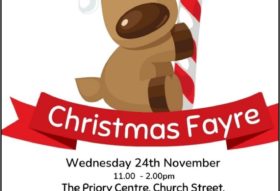 a poster for a christmas fayre event being held at The Priory Centre Leominster on 24th November 2021. The image shows a cartoon style dog reindeer character holding a red and whit candy cane sitting on a red ribbon banner.