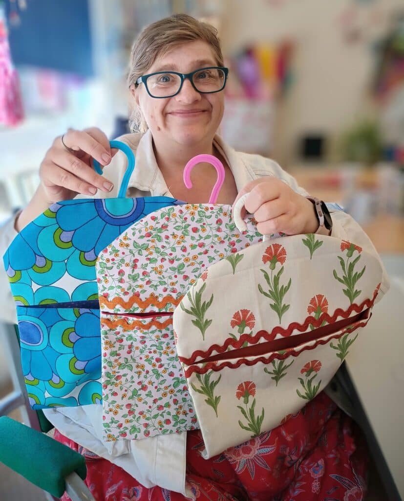 A woman holding up three peg bags that she has made from fabric material